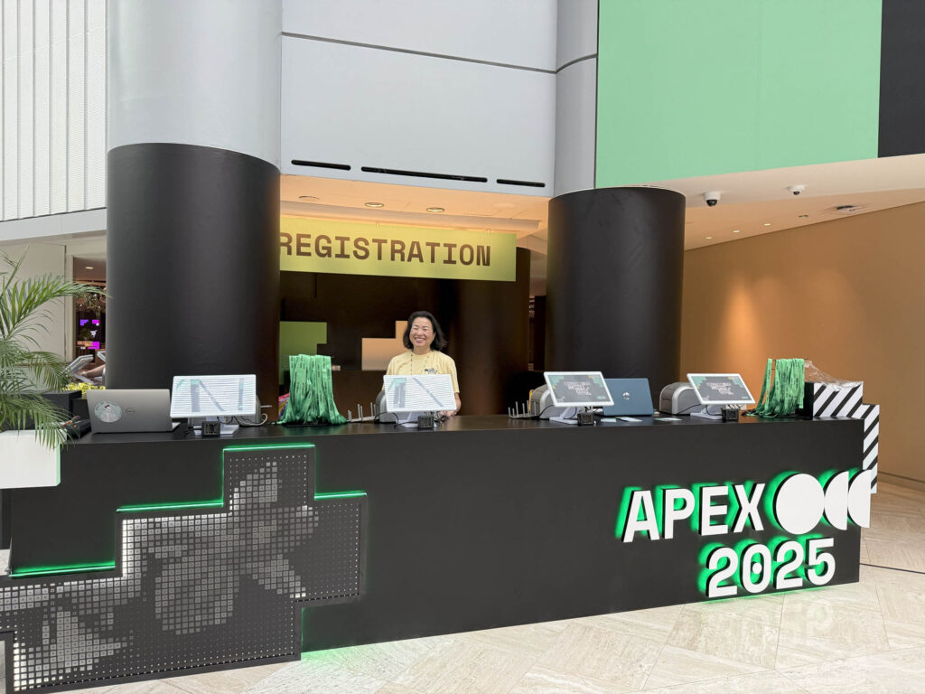A person stands behind a modern, black registration desk with green accents and 